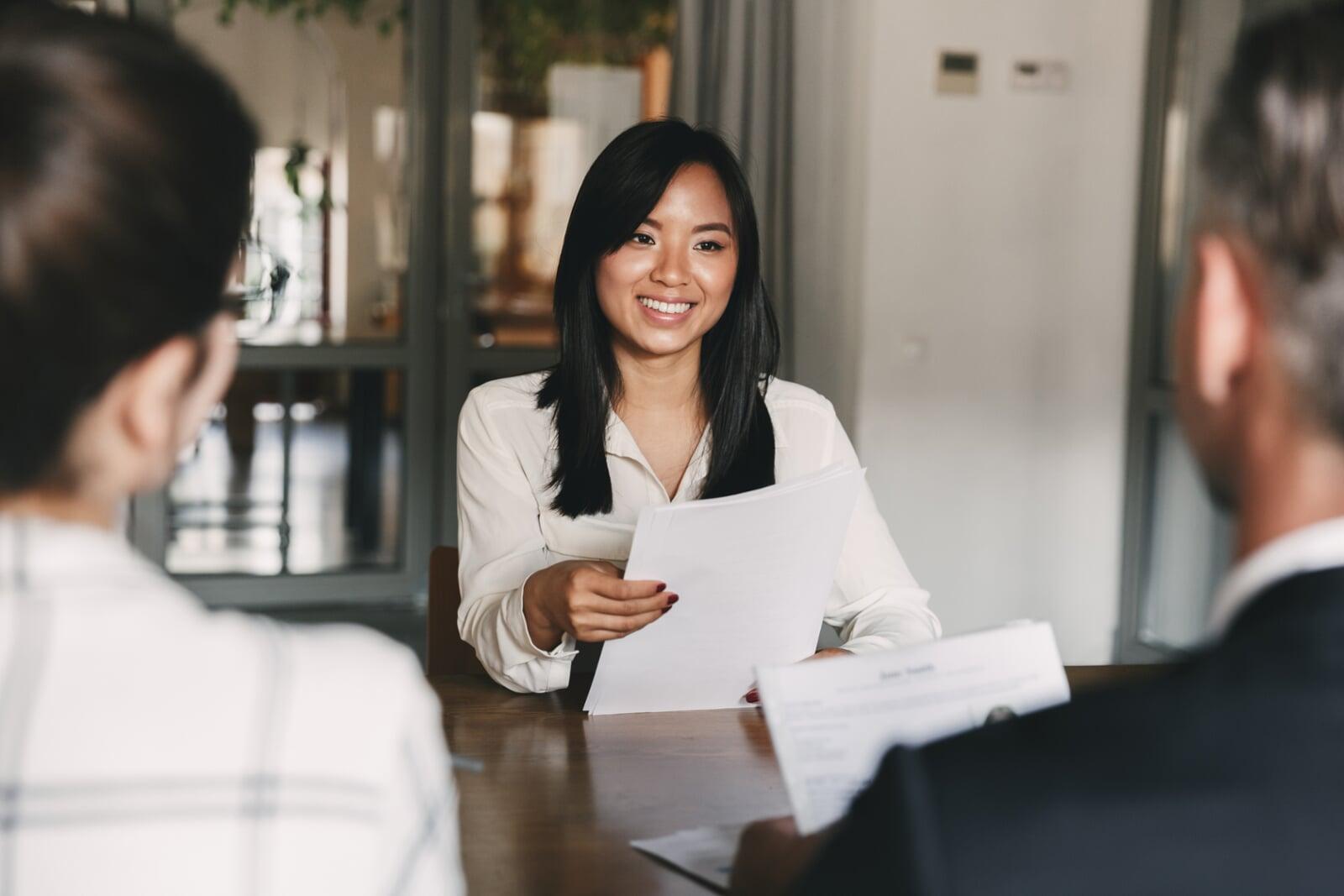 Three people sitting in an office, where one woman is being interviewed looking happy and optimistic about the potential opportunity.
