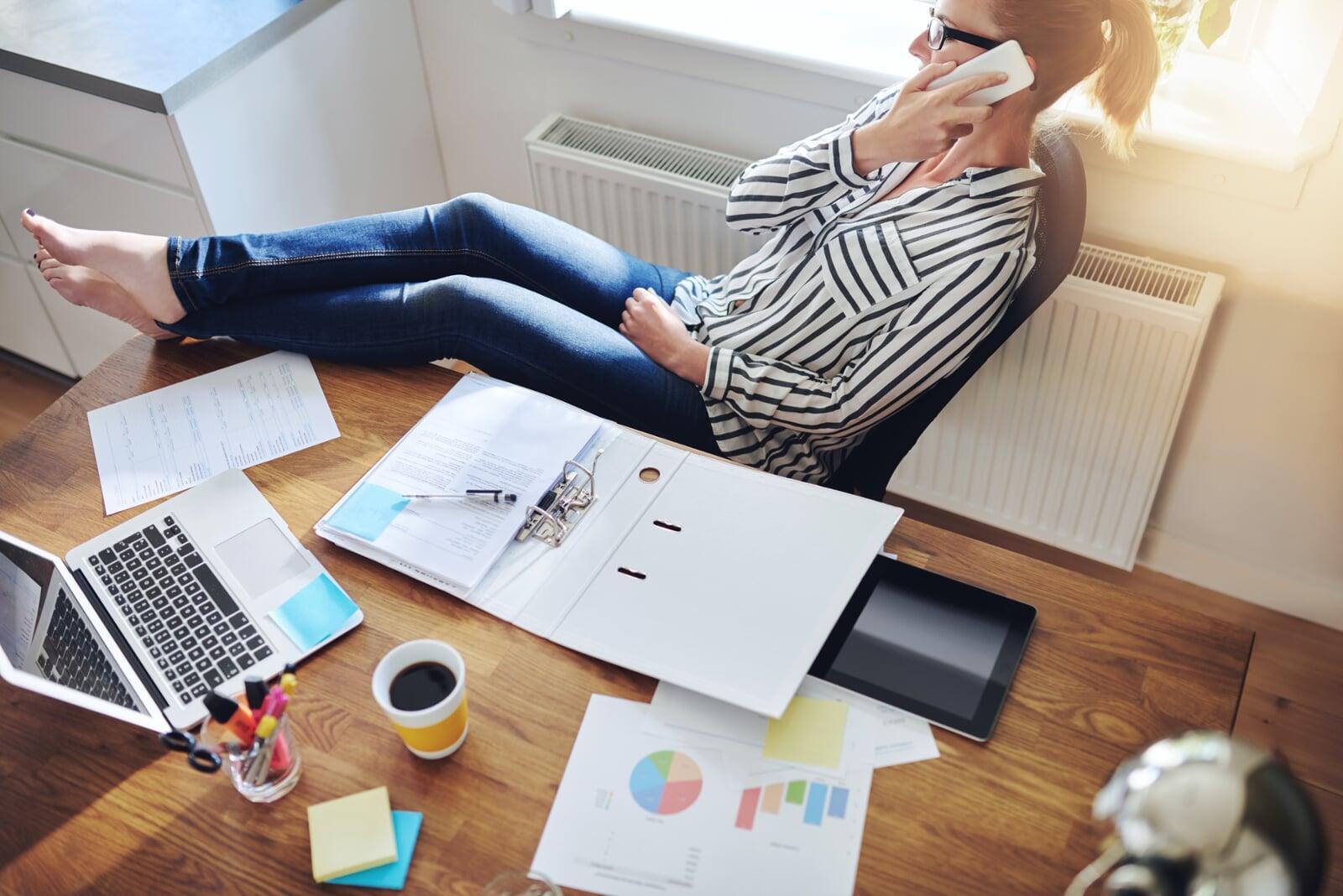 Woman sitting casually at a desk, on the phone, negotiating a salary.